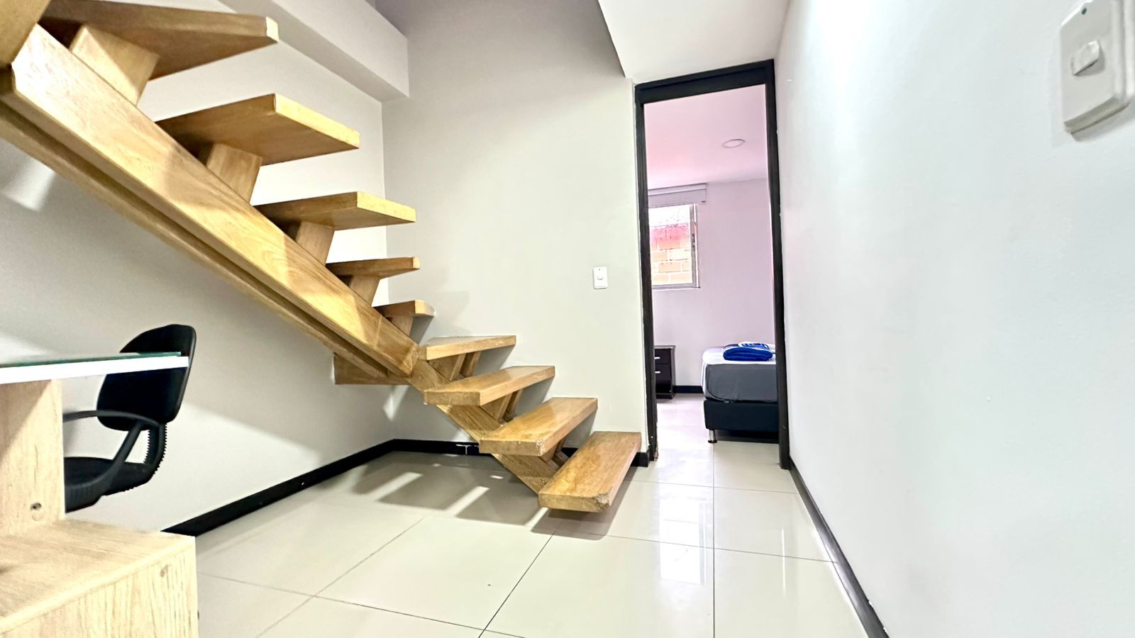 Un interior moderno con una escalera de madera que lleva a un dormitorio.