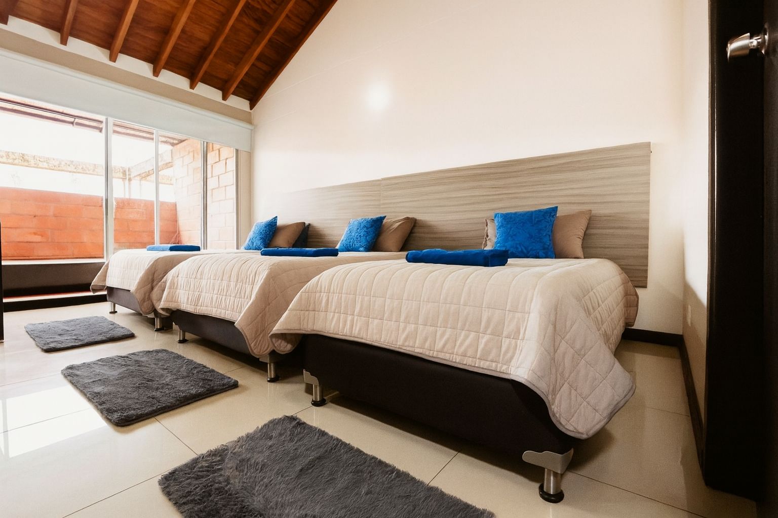 A hotel room with two beds, a large window, and a wooden ceiling.