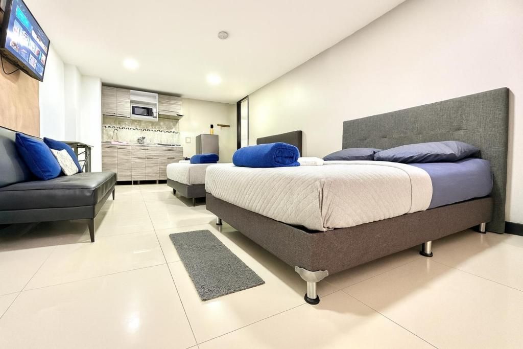 Quarto de hotel moderno com cama grande, sofá, televisão de tela plana e cozinha compacta ao fundo.