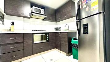 Una cocina con armarios de madera oscura, un refrigerador de acero inoxidable, un microondas y una estufa a gas.