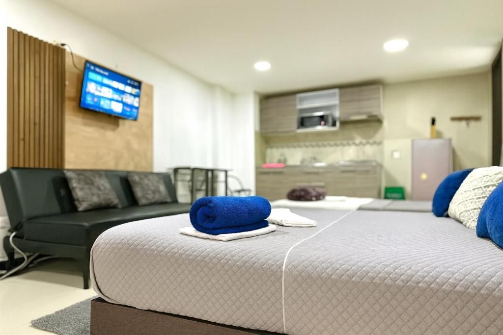 Una habitación de hotel moderna con cama, sofá, televisor montado en la pared y una zona de kitchenette.