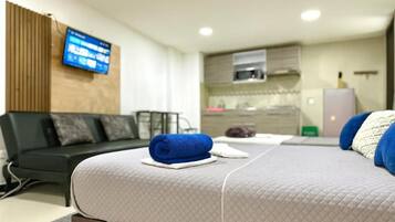 Una habitación de hotel moderna con cama, sofá, televisor montado en la pared y una zona de kitchenette.