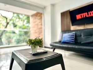 A modern living room with a black sofa, a television displaying 'NETFLIX', and a small table with a plant and remote control. - Tolupa Apartamentos (Medellín)