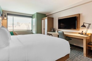 Habitación de hotel con una cama grande, un escritorio con televisor de pantalla plana, una silla y una lámpara de escritorio.
