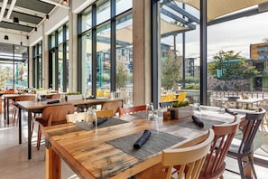 A modern restaurant with large windows, wooden tables, and chairs.