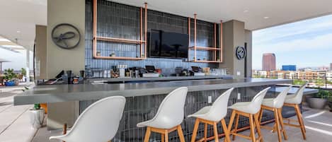 A modern bar area with a large countertop, multiple stools, and a television screen.