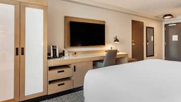Una habitación de hotel con cama, escritorio, televisor de pantalla plana, cafetera y lámpara.