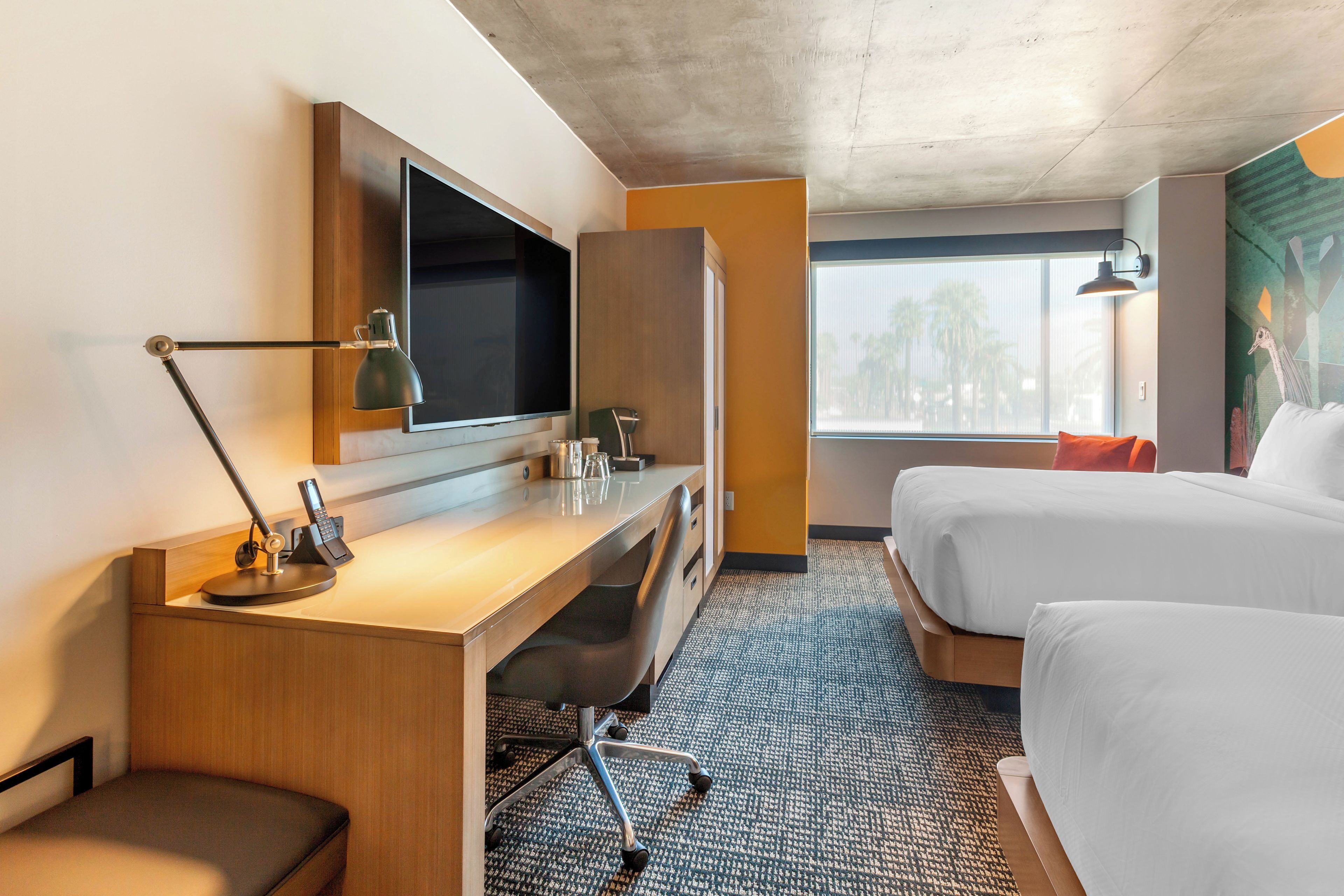 Habitación de hotel con escritorio, televisor de pantalla plana, cama, ventana con vistas y lámpara de pared.