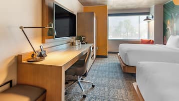 Habitación de hotel con escritorio, televisor de pantalla plana, cama, ventana con vistas y lámpara de pared.