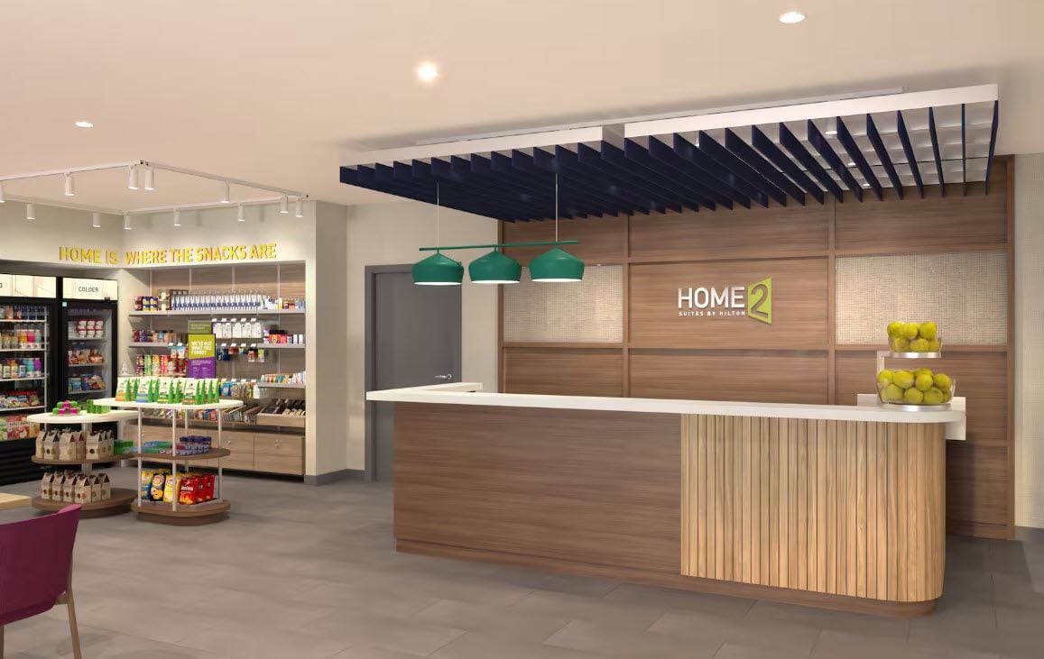 Un hall d’hôtel moderne avec un comptoir d’accueil, un espace où l’on peut prendre une collation et une enseigne indiquant « HOME 2 SUITES BY HILTON ».