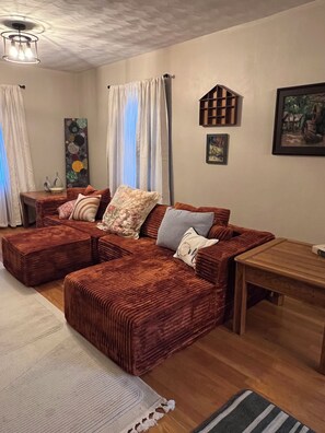 A cozy living room with a sectional sofa, a wooden coffee table, and a painting on the wall.