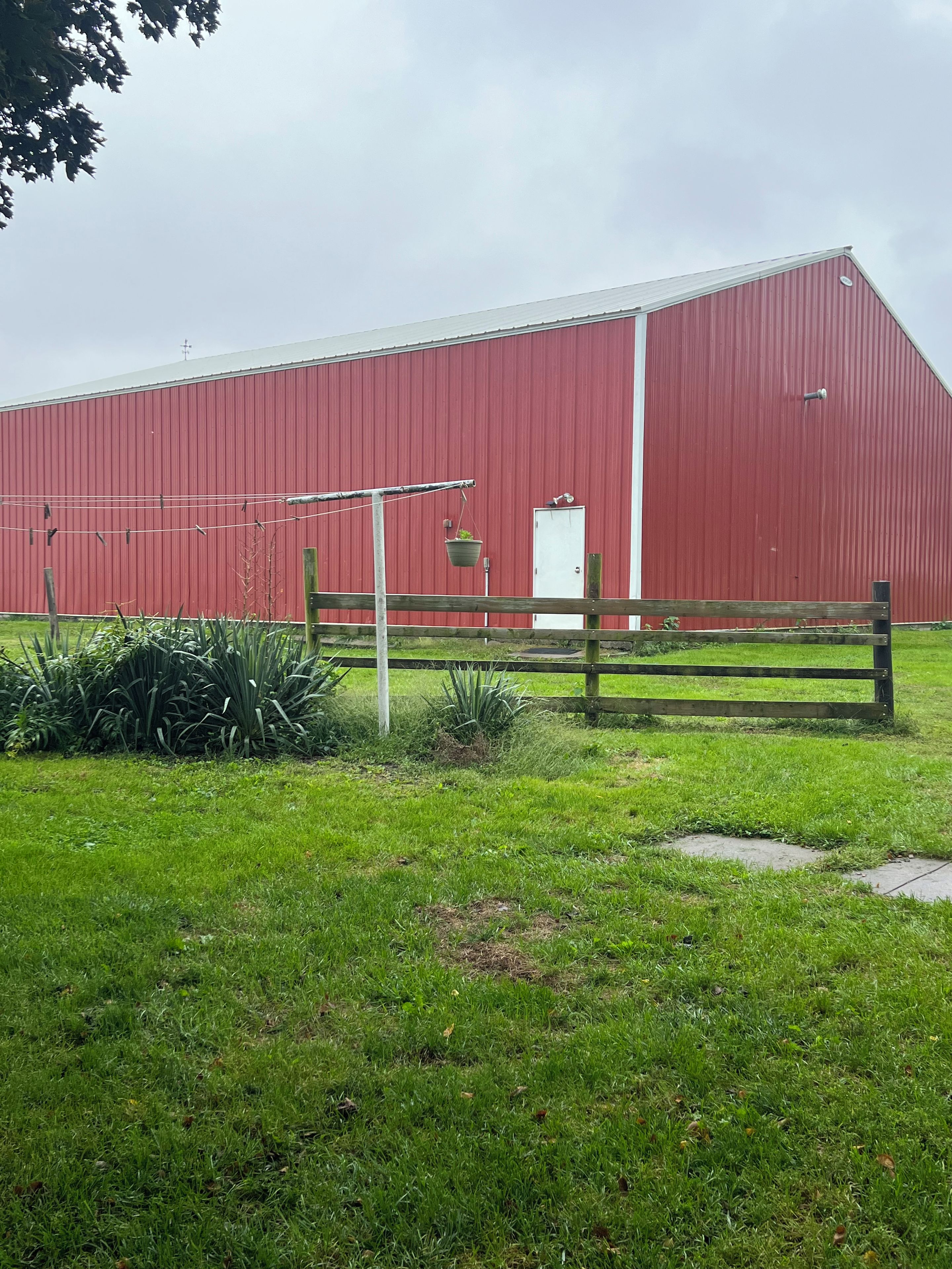 A red barn with a white door, surrounded by a grassy area with a wooden fence.