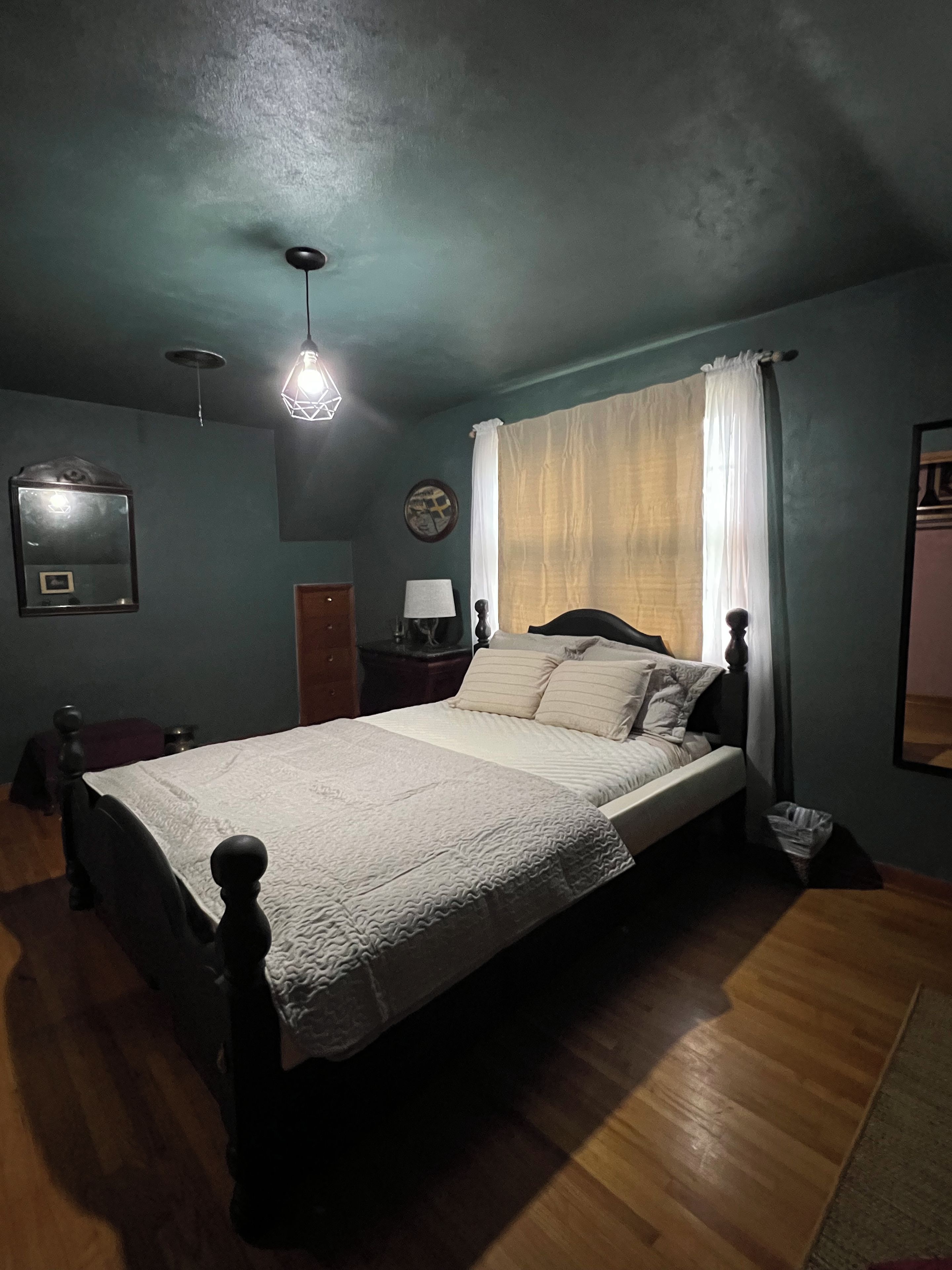 A bedroom with a bed, a nightstand, a lamp, a mirror, and a window with curtains.