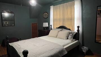 A bedroom with a bed, a nightstand, a lamp, a mirror, and a window with curtains.