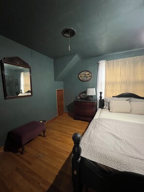 A bedroom with a bed, a bench, a dresser, a mirror, a clock, and a ceiling fan.