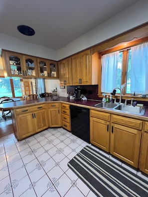A kitchen with wooden cabinets, a dishwasher, a sink, and a window with curtains.