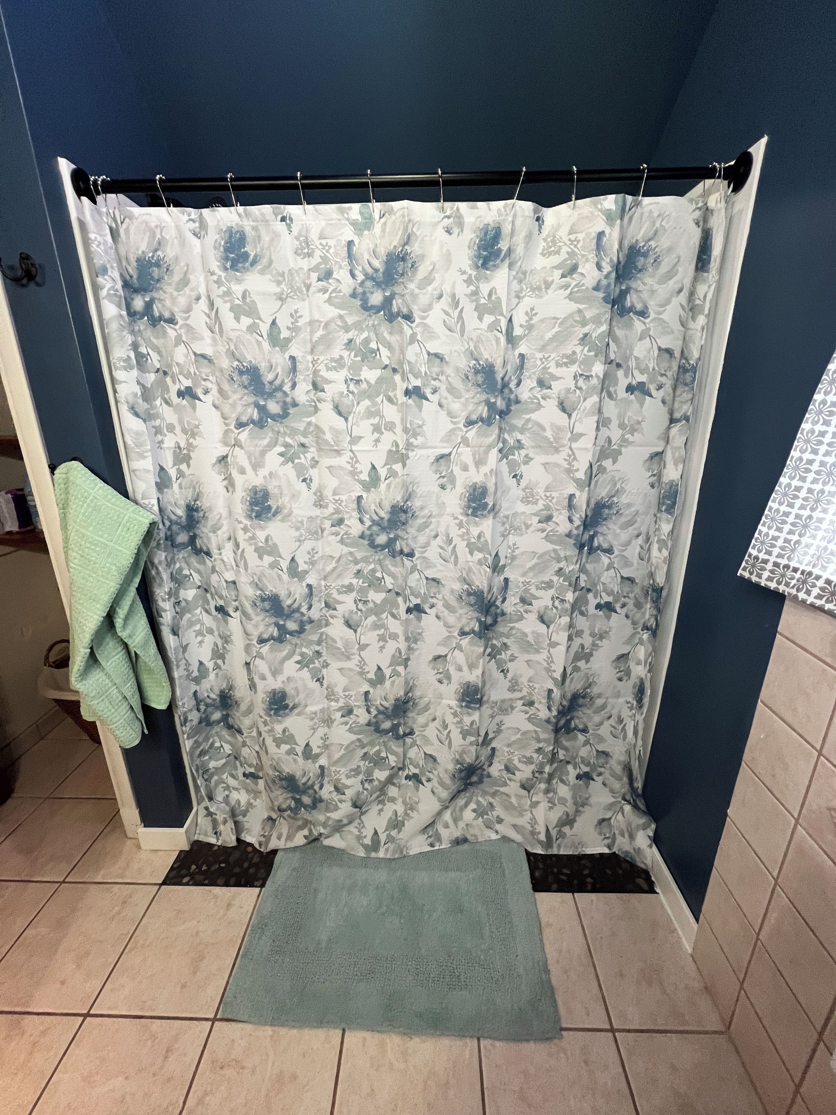A bathroom with a shower curtain featuring a floral pattern, a green bath mat, and a towel rack with a green towel.