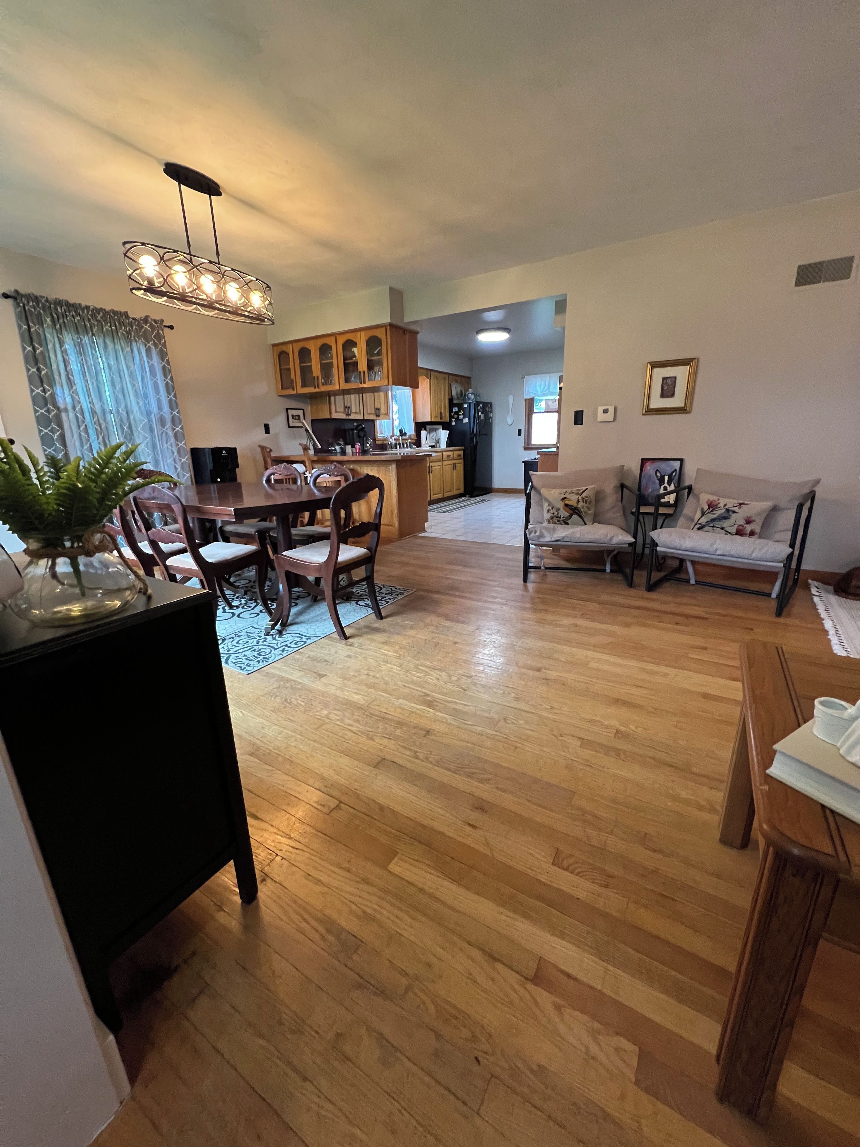 A spacious living area with a wooden dining table, chairs, a sofa, and a kitchen in the background.