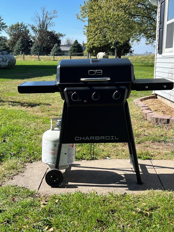 A Charbroil gas grill with a side burner, a propane tank, and a metal stand.
