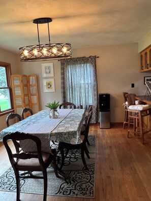 A dining area with a table set for four, surrounded by chairs, a potted plant, and a decorative rug.