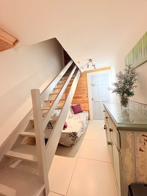 Eine Treppe führt zu einem Schlafzimmer mit einem Bett, einem Schminktisch und einer Tür.