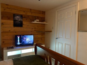 Una habitación con una televisión sobre una pared de madera, una puerta blanca y una cama con una colcha verde.