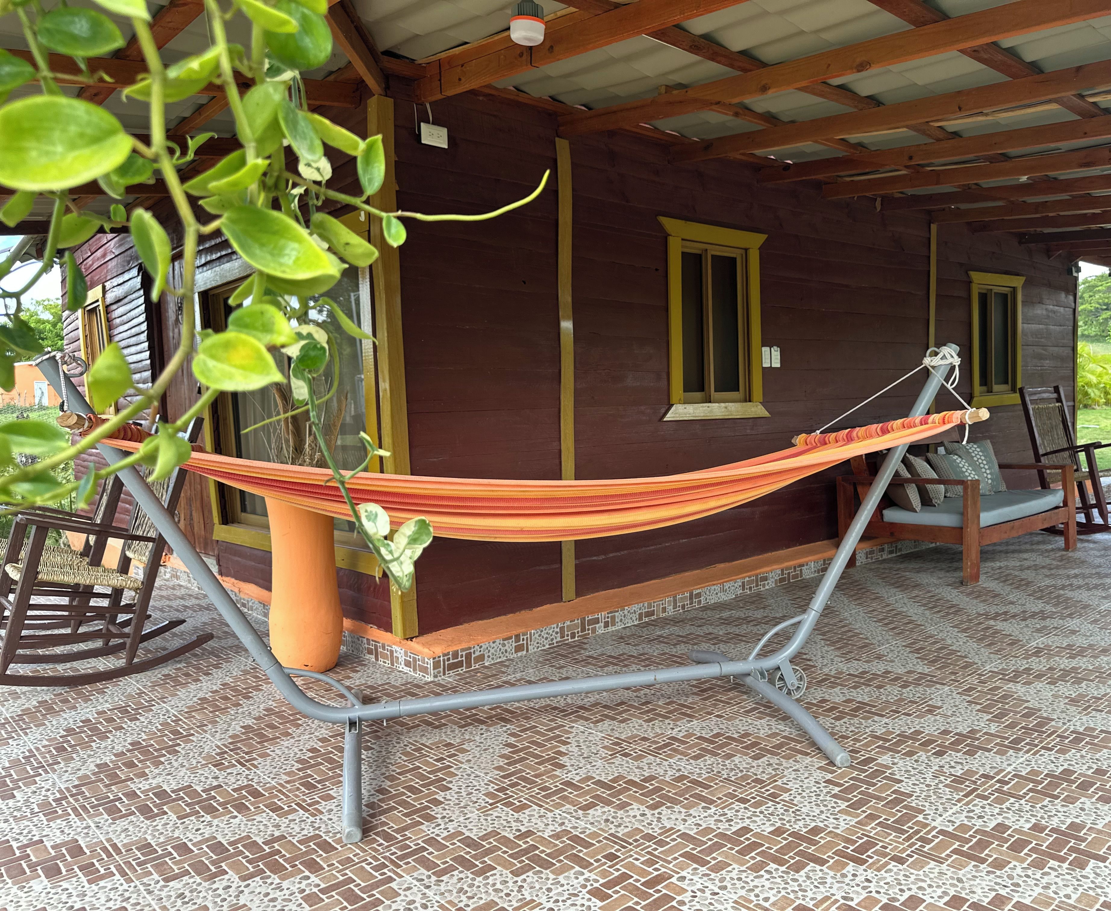 Eine Hängematte auf einer Veranda mit Fliesenboden, einem Schaukelstuhl und einem Blumentopf.