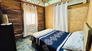 A single bed with a blue and white bedspread, wooden walls, and a corrugated metal roof.