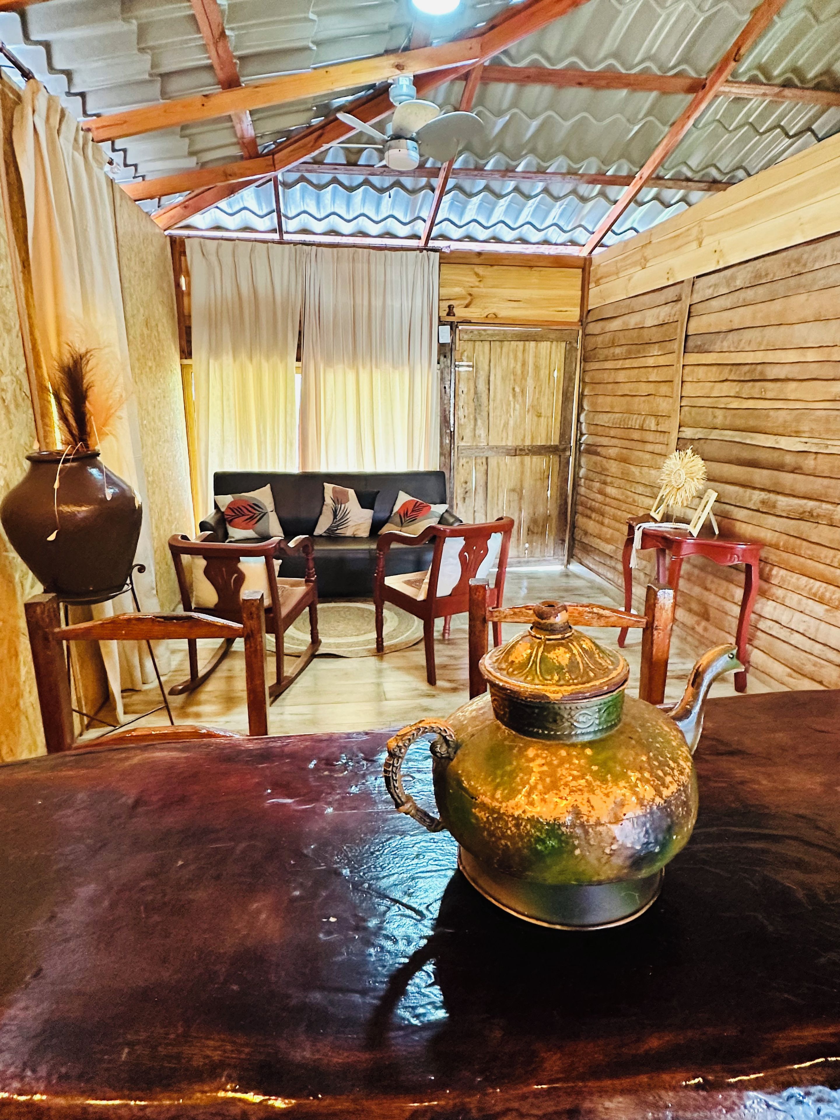 A rustic interior with a wooden table, a sofa, and chairs. A decorative teapot is on the table.