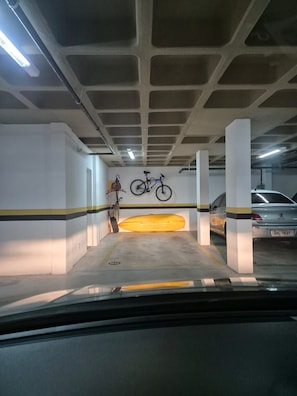 A parking garage with concrete pillars, a yellow kayak, and a bicycle. - Apto 2 quartos em resort a passos da praia – Cachoeira do Bom Jesus (Florianópolis)