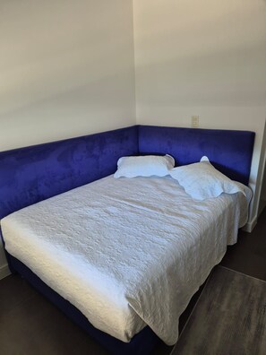 A bed with a blue headboard in a room with white walls. - Apto 2 quartos em resort a passos da praia – Cachoeira do Bom Jesus (Florianópolis)