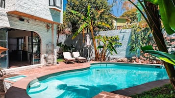 A swimming pool with lounge chairs, a stone wall, and tropical plants.