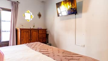 Une chambre à coucher avec un lit, un téléviseur fixé au mur, une commode et une fenêtre avec des rideaux.