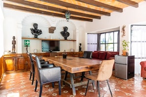 A dining area with a wooden table, chairs, and a sofa. There is a television, a refrigerator, and decorative items on the walls. - Santoria Restaurante & Hotel (San Miguel de Allende)