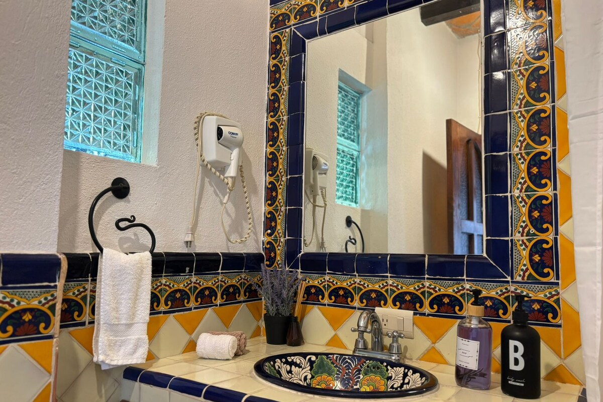Ein Badezimmer mit dekorativer Fliesenwand, einem Waschtisch mit floralem Dekor, einem Handtuchhalter und einem Spiegel mit Zierrahmen.