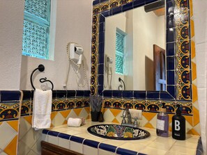Ein Badezimmer mit dekorativer Fliesenwand, einem Waschtisch mit floralem Dekor, einem Handtuchhalter und einem Spiegel mit Zierrahmen.
