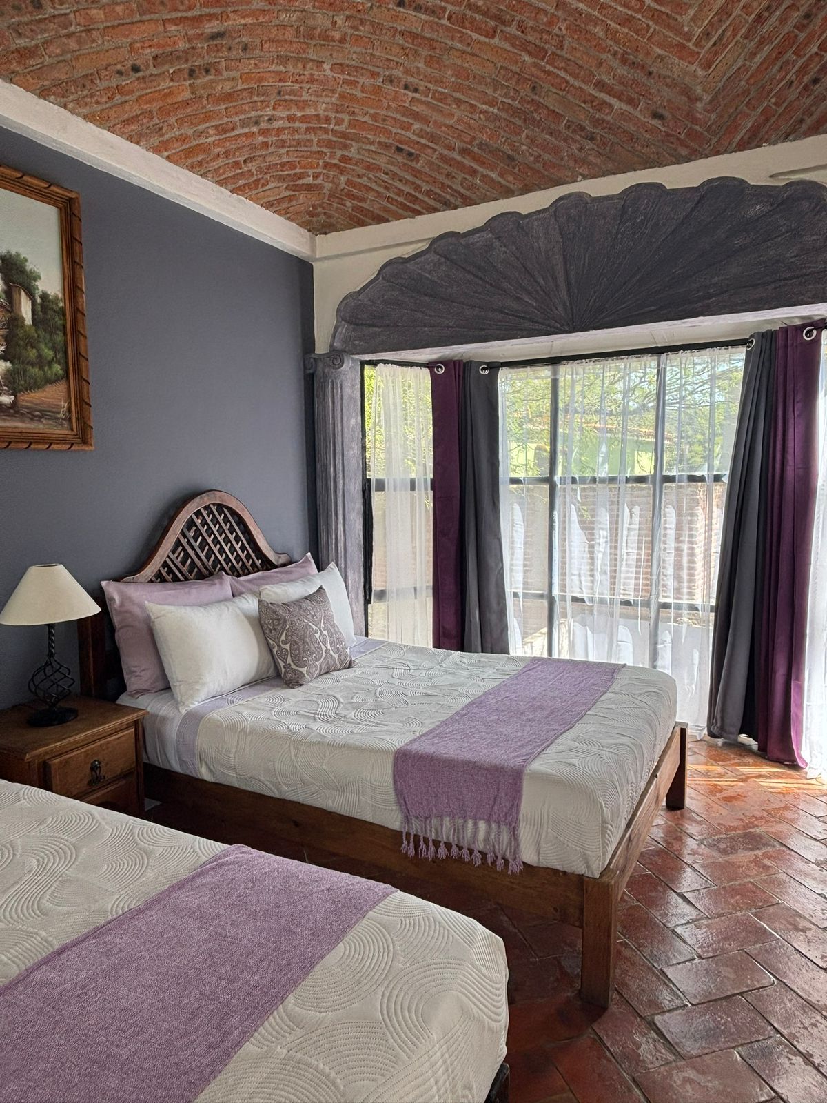 Quarto com duas camas, cabeceira de madeira, mesa de cabeceira e janela com cortinas.
