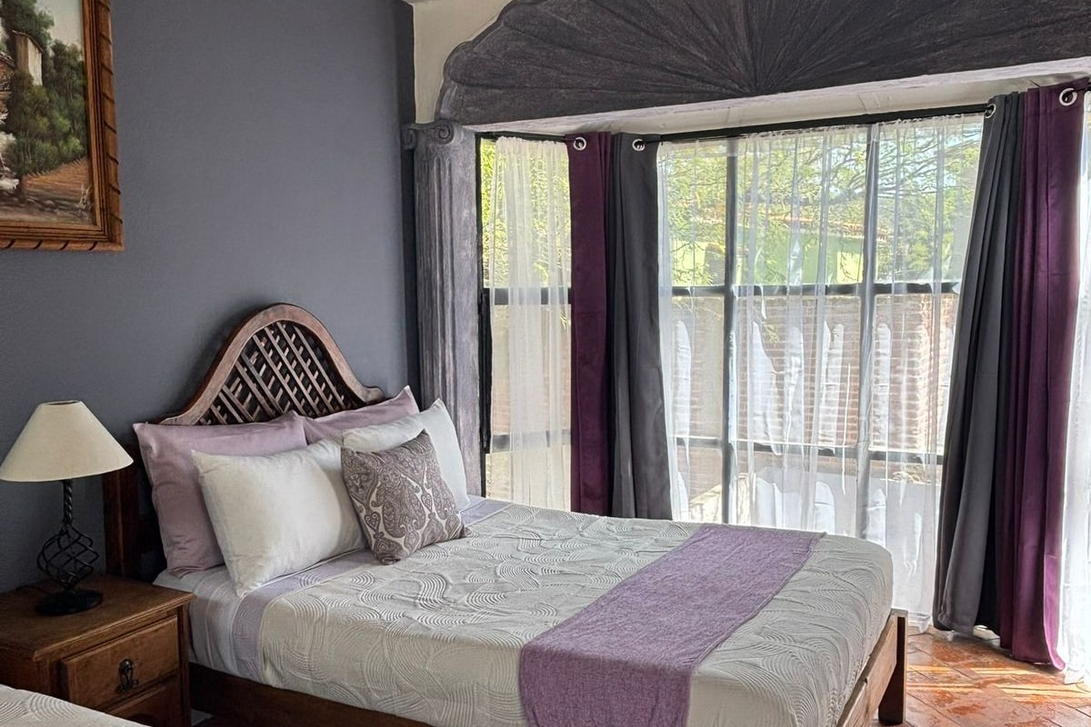 Quarto com duas camas, cabeceira de madeira, mesa de cabeceira e janela com cortinas.