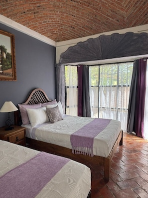 Quarto com duas camas, cabeceira de madeira, mesa de cabeceira e janela com cortinas.