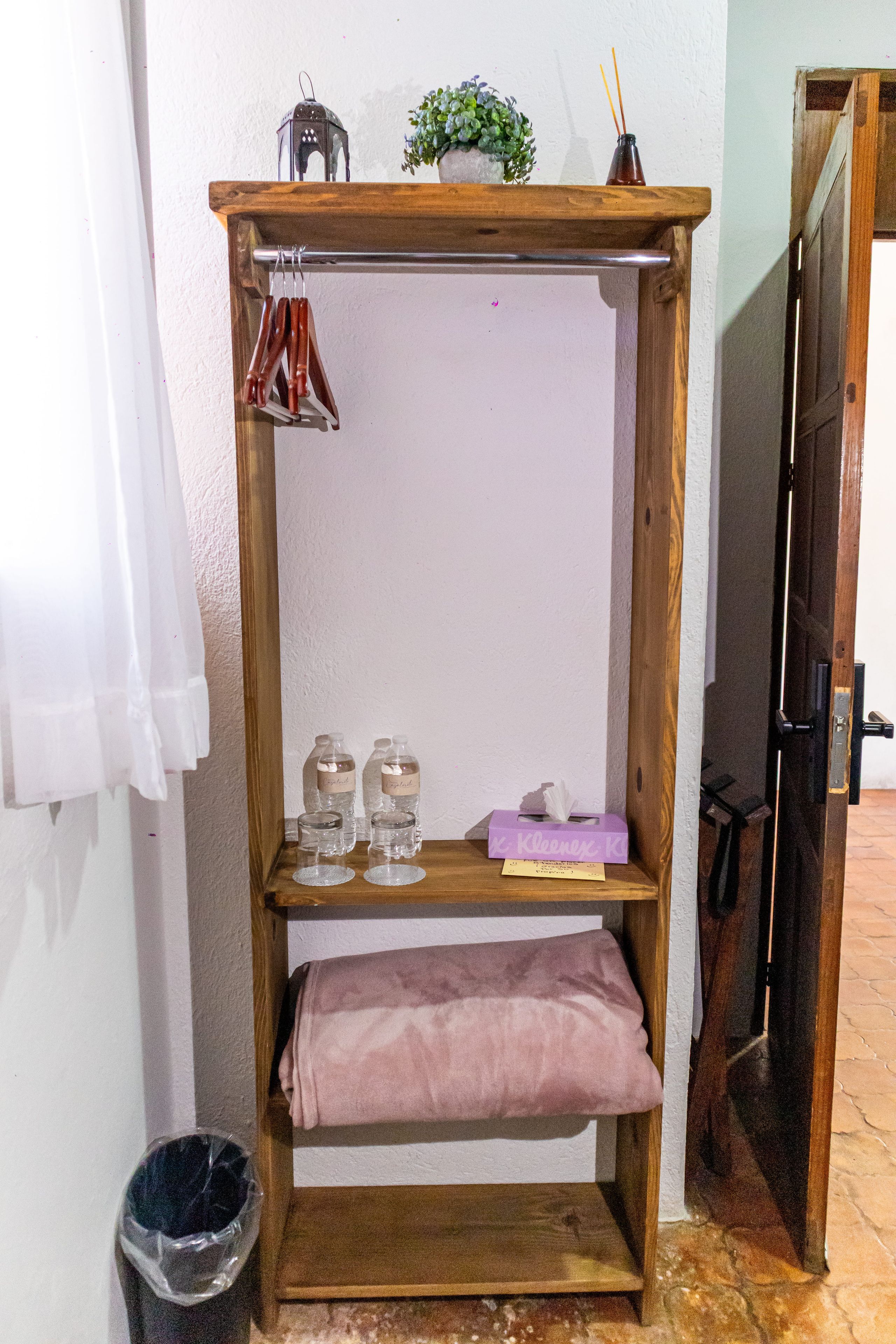 Une étagère en bois avec des vêtements suspendus, une petite plante et une boîte de mouchoirs.