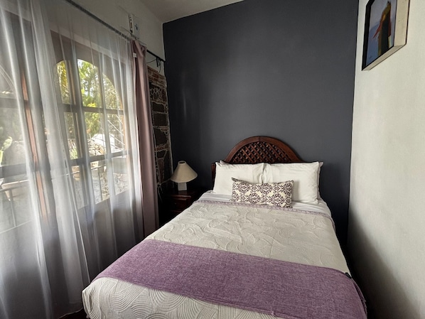 Un dormitorio con cama, mesita de noche, lámpara y ventana con cortinas.