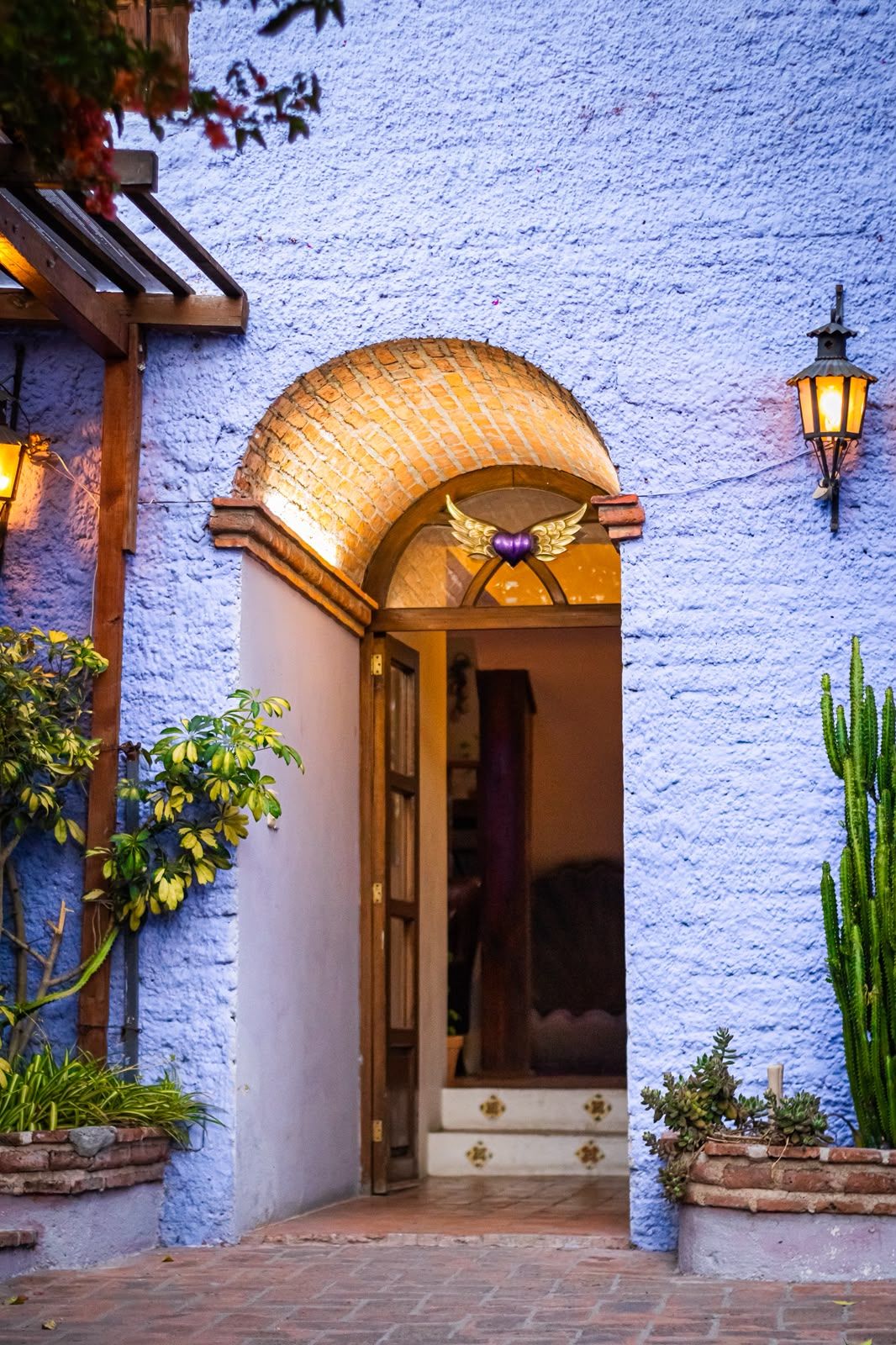 Una entrada de edificio con un arco de ladrillo, un emblema decorativo sobre la puerta y un accesorio de luz fijado a la pared.
