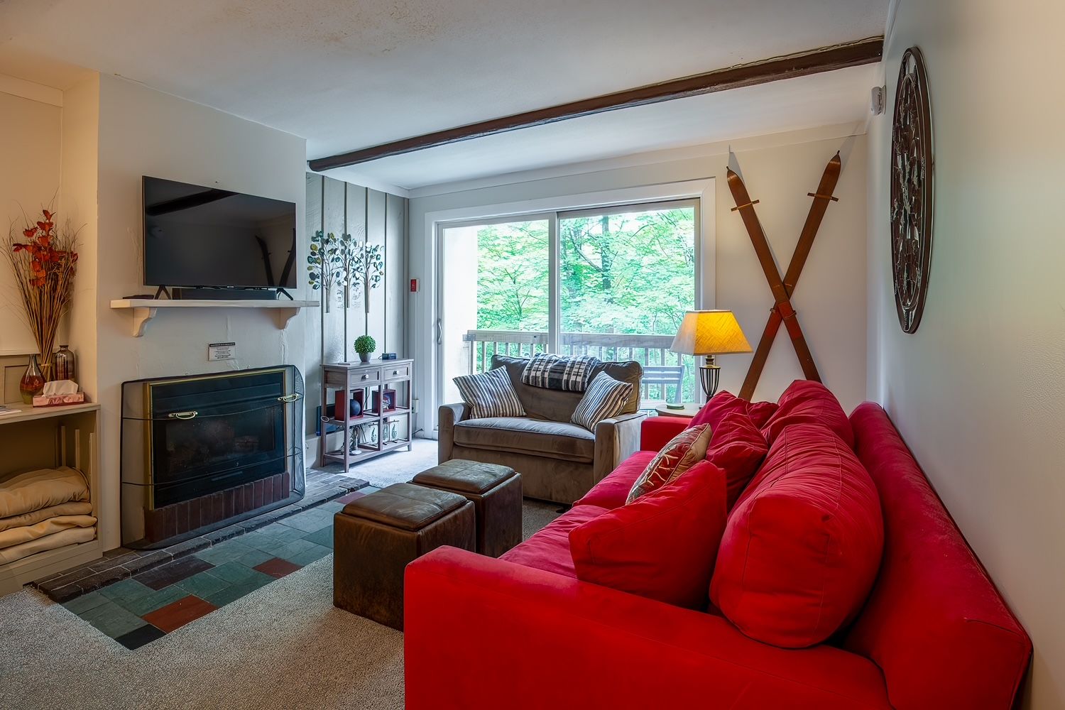 A living room with a fireplace, a television, a sofa, and a window with a view of trees.