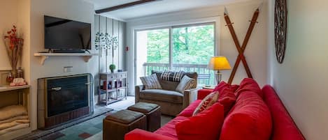 A living room with a fireplace, a television, a sofa, and a window with a view of trees.