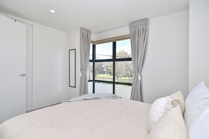 A bedroom with a large bed, a window with curtains, and a door. - City-side Riccarton, Walk to Mall - Matai St West (Riccarton)