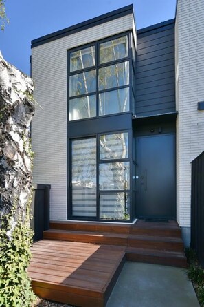 A modern two-story building with large windows, a wooden deck, and a concrete pathway. - City-side Riccarton, Walk to Mall - Matai St West (Riccarton)