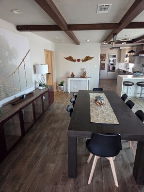 A modern dining area with a long table, chairs, and a kitchen in the background. - Modern cabin style home in the heart of San Antonio. (San Antonio)