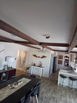 Une cuisine moderne dotée d’un îlot central, de poutres en bois au plafond et d’un coin repas avec une longue table et des chaises.