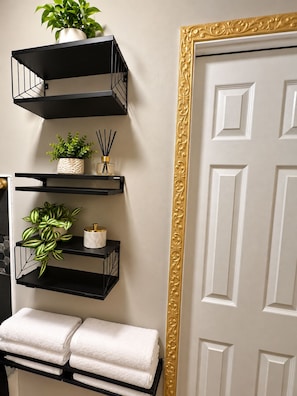 A bathroom with black metal shelves, a white door with a gold frame, and white towels. - Just Minutes From Downtown, Cleveland Clinic & University Circle, Free Parking (Cleveland)