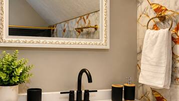 A bathroom with a white sink, black faucet, and a mirror with a gold frame.